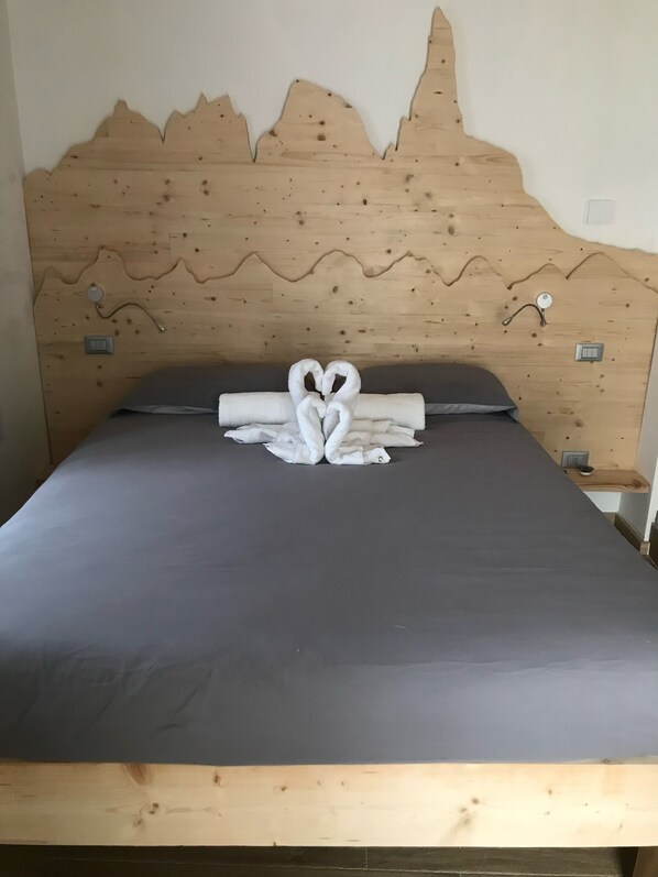 A bed with a wooden headboard, a heart-shaped towel arrangement, and a grey mattress.