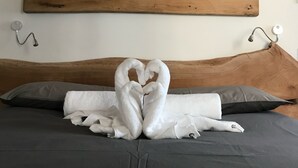 A bed with a wooden headboard, a painting of a mountain landscape, and a heart-shaped towel arrangement on the bed.