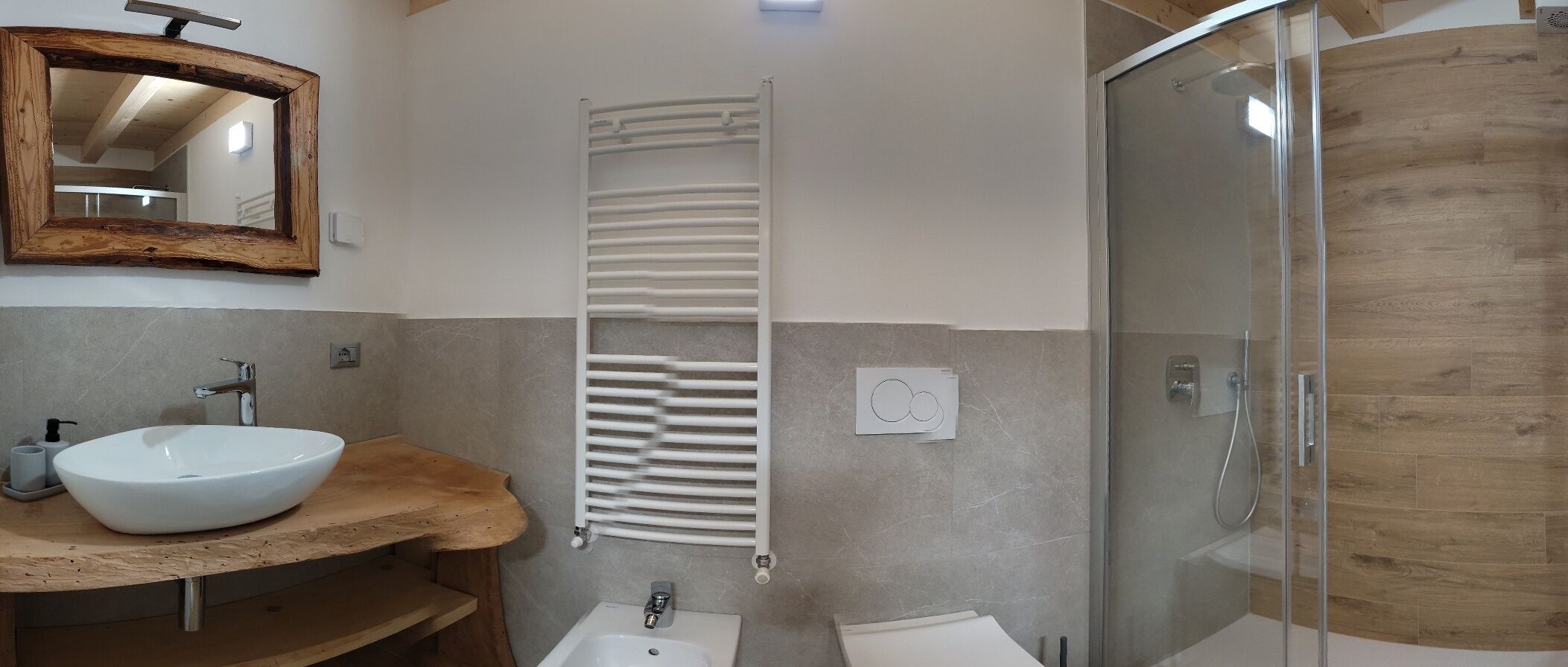 Un baño con tocador de madera, un lavabo blanco, un perchero para toallas, una ducha con puerta de cristal y un espejo con marco de madera.