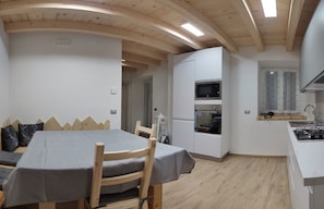 A compact room with a dining table, chairs, a built-in oven, and a small kitchenette. - Profumo di Legno - CODICE CIPAT 022139-AT-010022 (Roncogno di Pergine Valsugana)