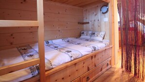Une chambre avec un lit superposé en bois, un petit miroir rond et une fenêtre.