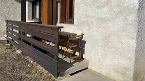Un banc et une table en bois se trouvent à l’extérieur d’un bâtiment dont le mur présente une texture particulière et qui est doté de volets en bois.