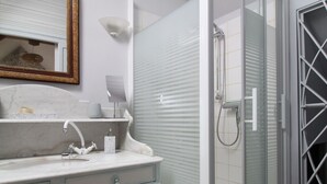 Een badkamer met een marmeren wastafel, een spiegel met decoratieve lijst, een zeepdispenser en een douche met glazen deur.