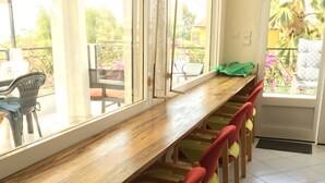 A long wooden table with multiple chairs, a window with a view of greenery, and a door with a mat. - VILLA 4 bedrooms facing the sea swimming pool garden terrace parking comfort for 12 (M'Bour)