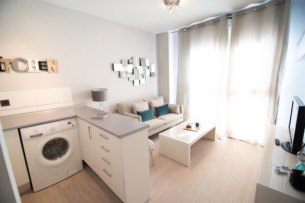 A modern living room with a washing machine, a sofa, a coffee table, and a TV.