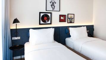 A hotel room with two beds, a nightstand, a lamp, and wall art including a vinyl record and framed pictures.
