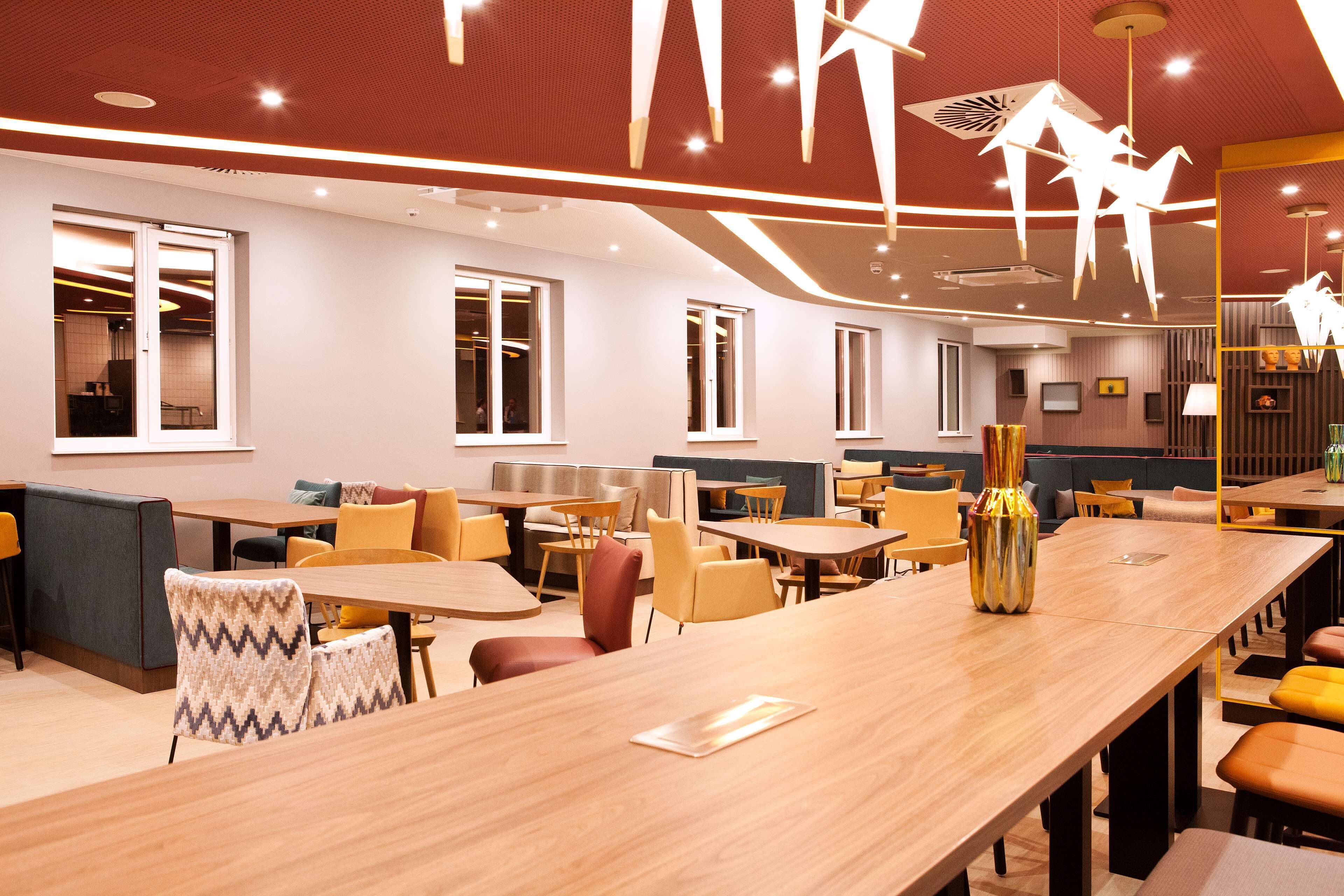 A modern dining area with wooden tables and chairs, large windows, and contemporary lighting fixtures.