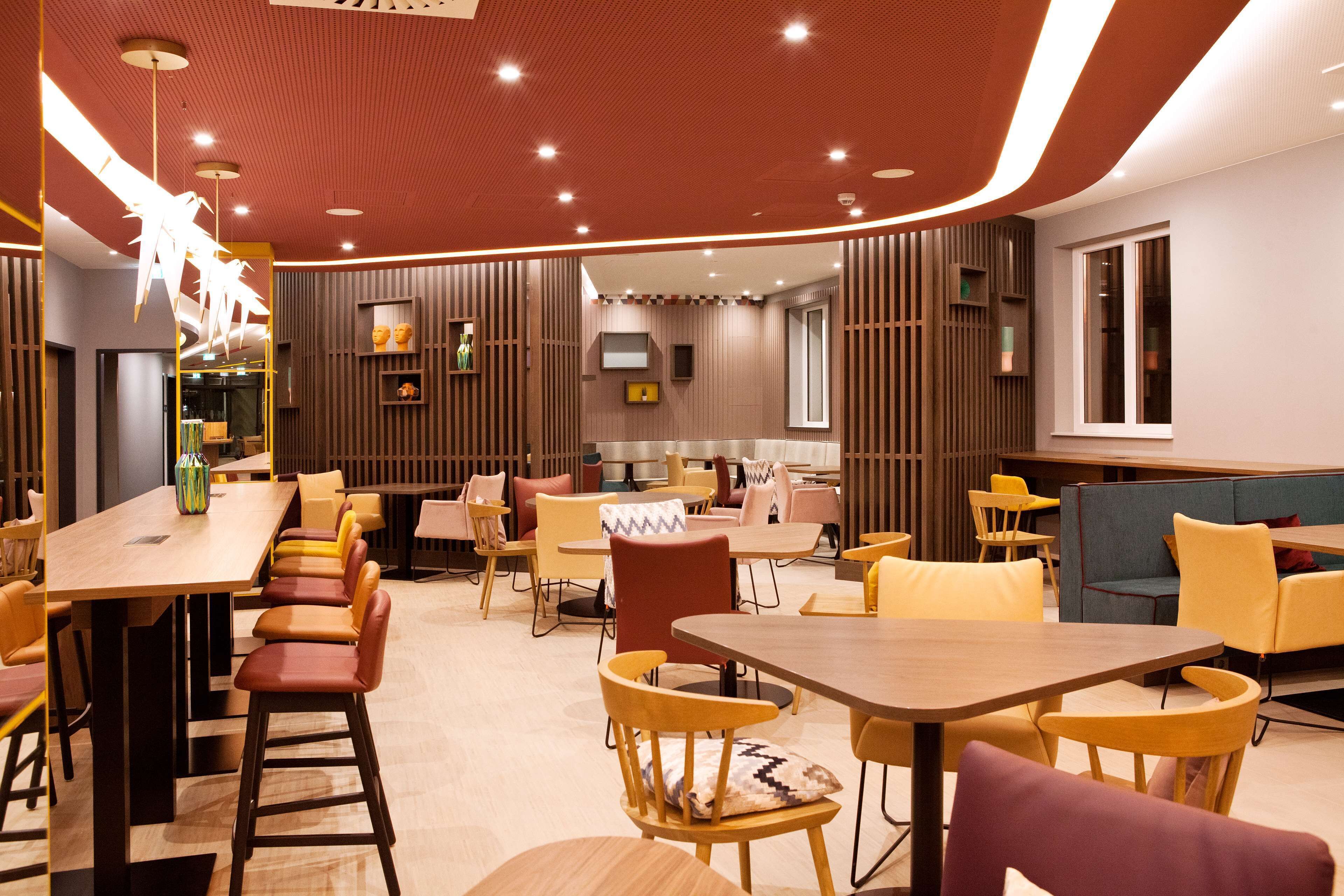 Een moderne eetruimte met houten tafels en stoelen, een bar en een zithoek met banken en fauteuils.