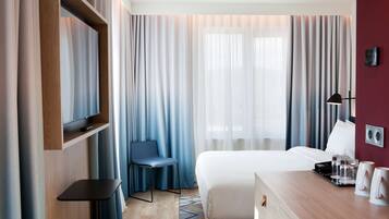 A hotel room with a bed, a desk, a chair, a TV, and curtains.