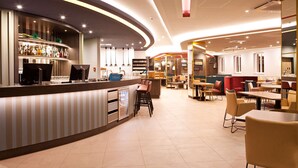 Un hall d’hôtel moderne avec un comptoir d’accueil incurvé, un espace bar et des coins salon.