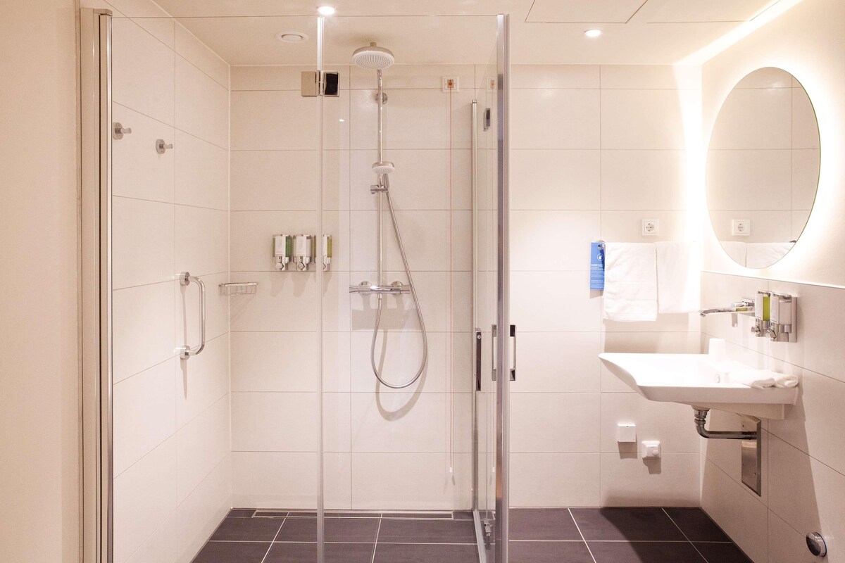 Ein modernes Badezimmer mit einer Duschkabine aus Glas, einem Waschbecken mit Spiegel und gefliesten Wänden.