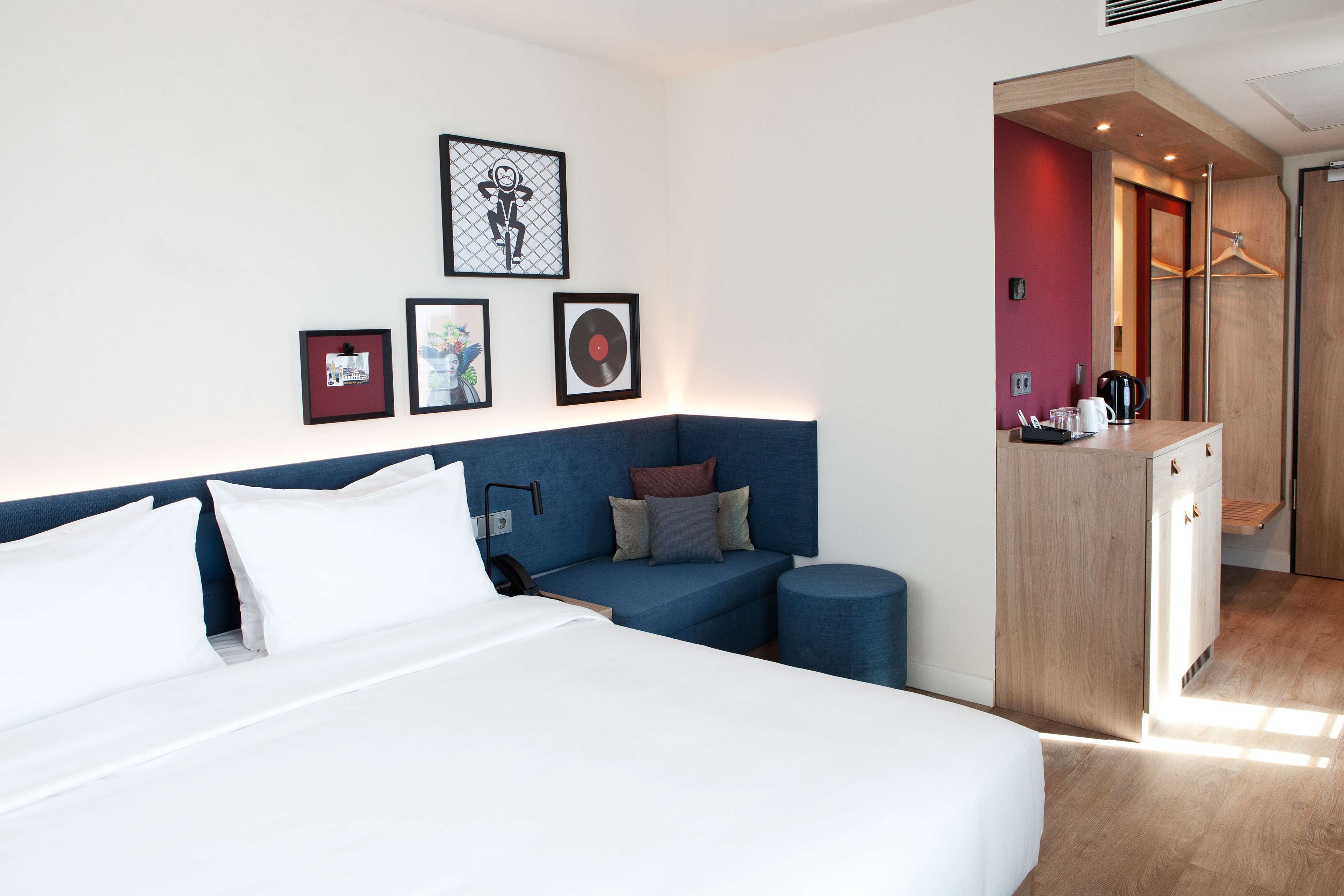 A modern hotel room with a large bed, a blue sofa, a small round table, and a wardrobe.
