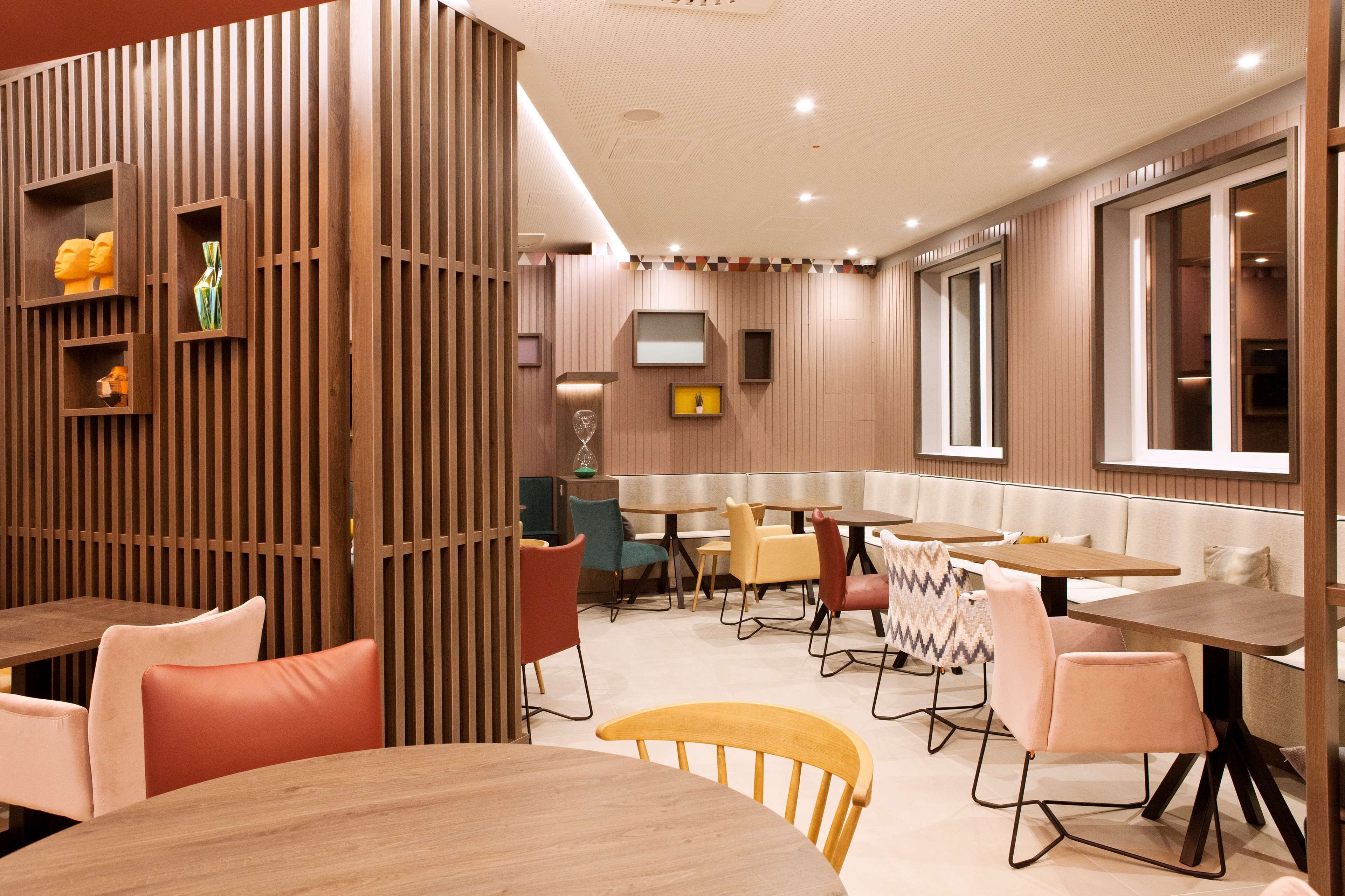 Un comedor moderno con paneles de madera, varias mesas y sillas, y un ventanal que proporciona luz natural.