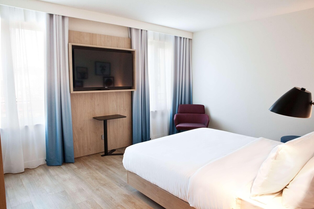 Ein Hotelzimmer mit Bett, Wandfernseher, Schreibtisch und Stuhl.