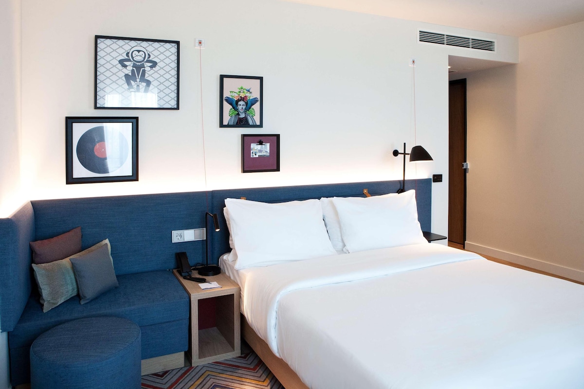 Een hotelkamer met een bed, een bank en een nachtkastje. Er hangen ingelijste foto's aan de muur.