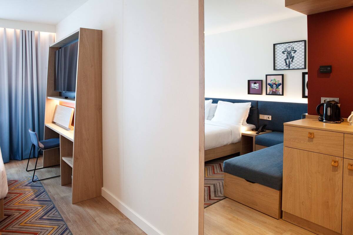 Ein Hotelzimmer mit Bett, Schreibtisch, Stuhl, Kleiderschrank und Fernseher.