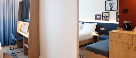 Quarto de hotel com cama, escrivaninha, cadeira, guarda-roupa e televisão.