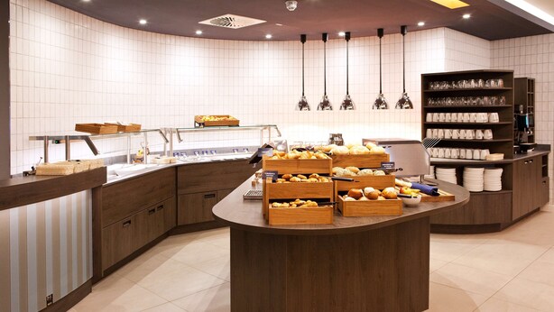 Une cuisine moderne dotée d’un îlot central où sont exposés des pâtisseries, ainsi que d’un coin café et d’une étagère où sont rangés avec soin des verres.