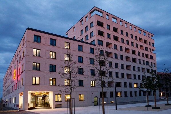 Un hotel de varios pisos con diseño moderno, que destaca por su entrada iluminada con señalización.