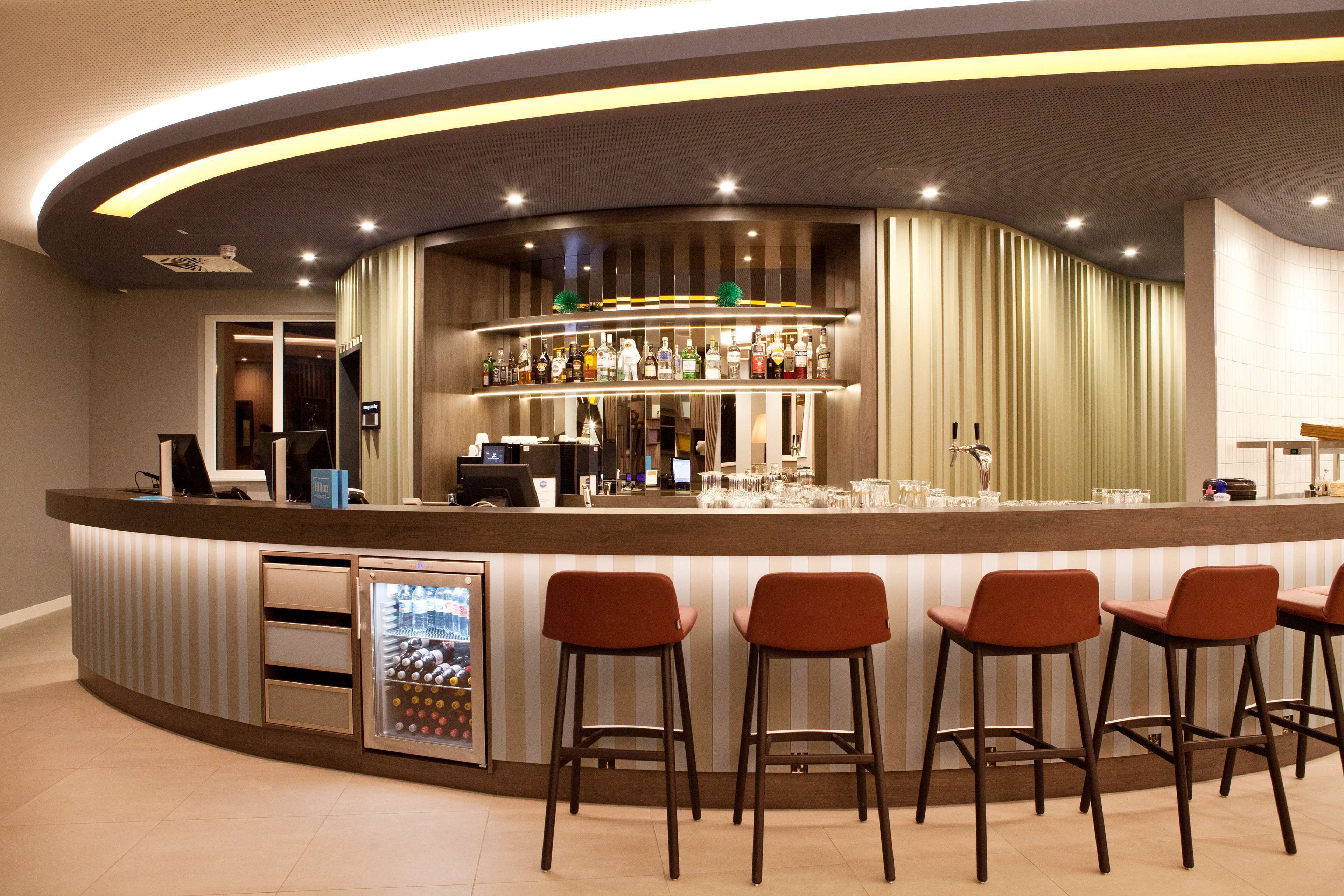 A bar area with a curved counter, bar stools, and a refrigerated display case.