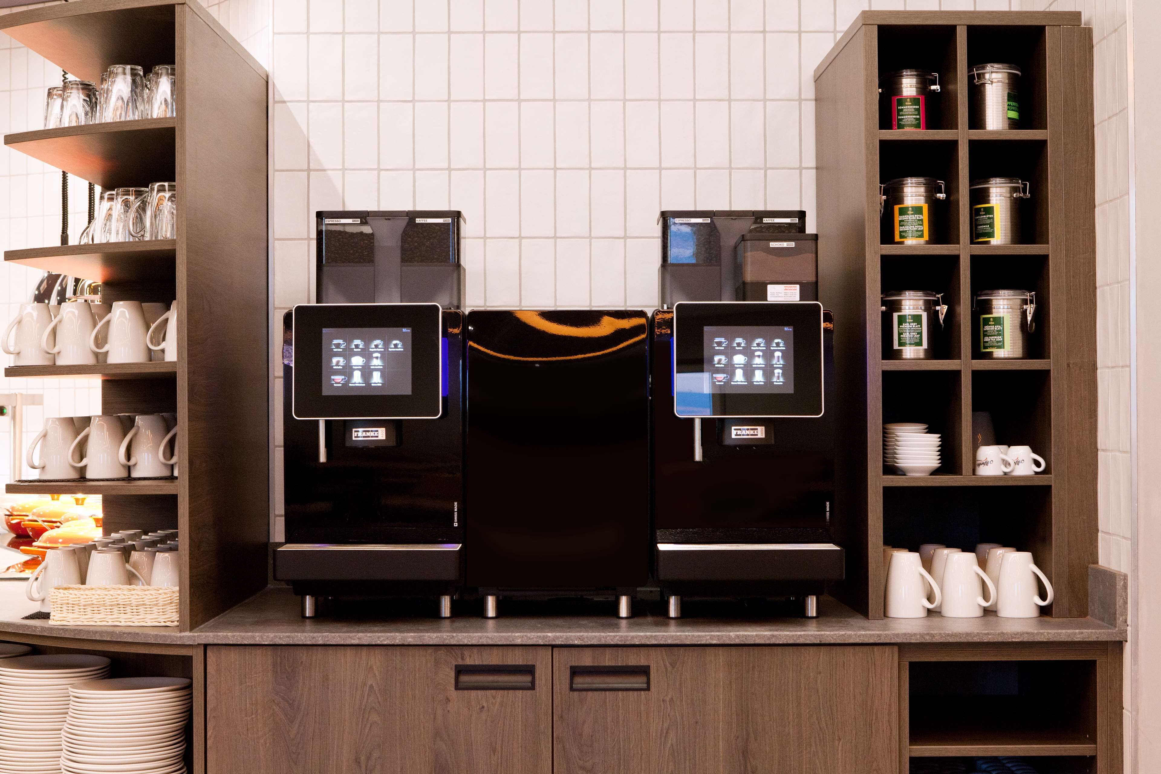 Un espace dédié au café, équipé de deux machines à expresso, d’un moulin à café et d’une étagère où sont rangées des tasses et des mugs.
