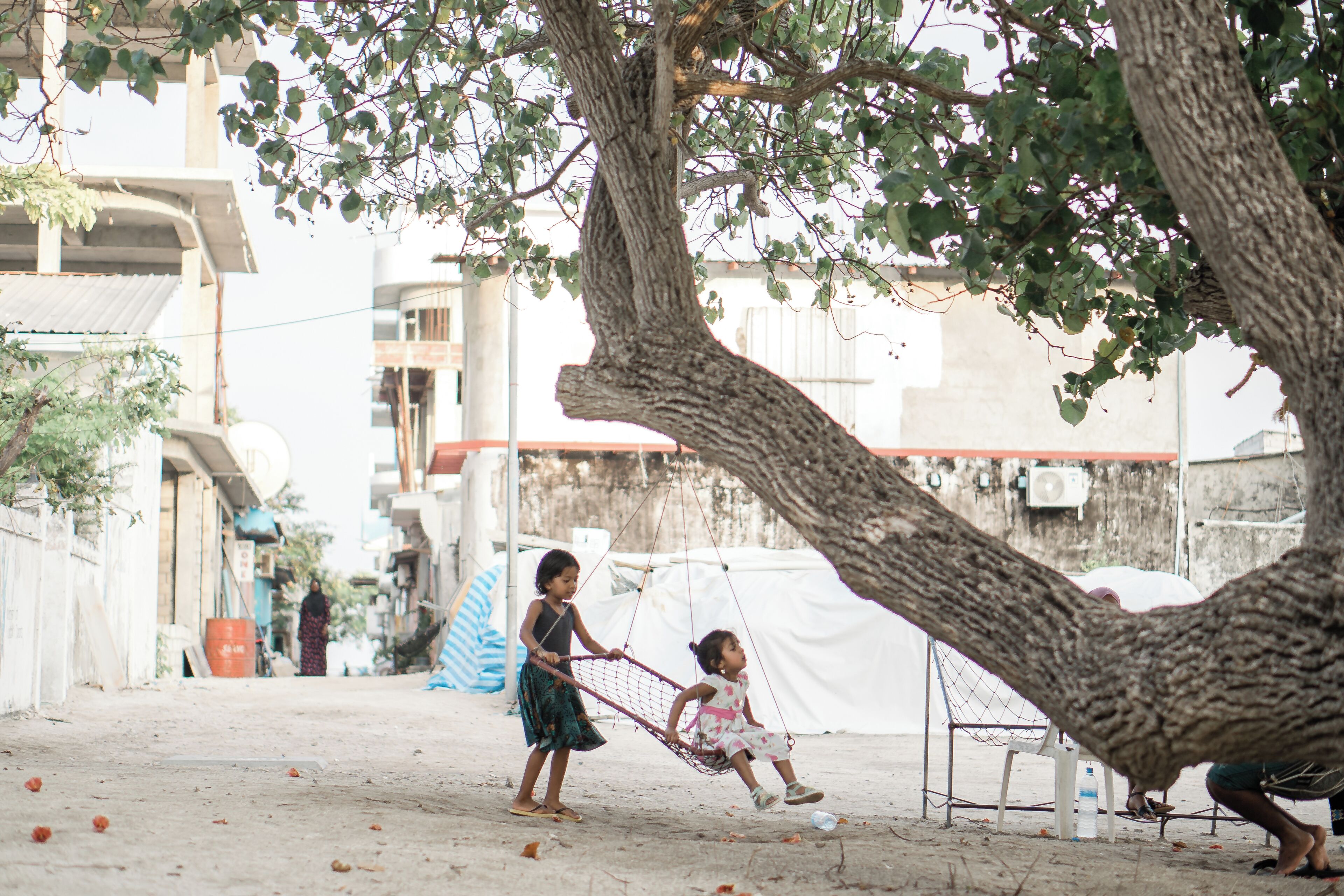 A tree-lined street with a swing set and a white tent in the background.