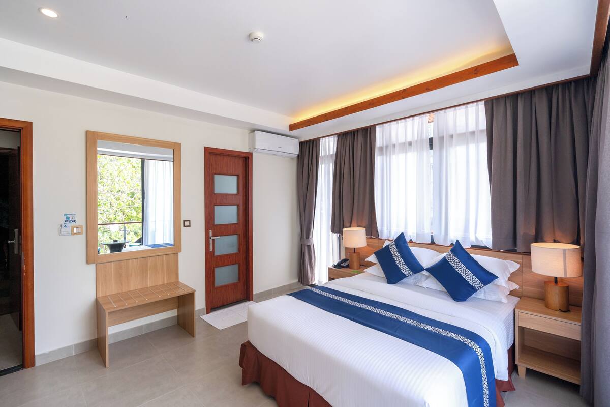 A hotel room with a large bed, bedside lamps, a wooden bench, and a window with curtains.