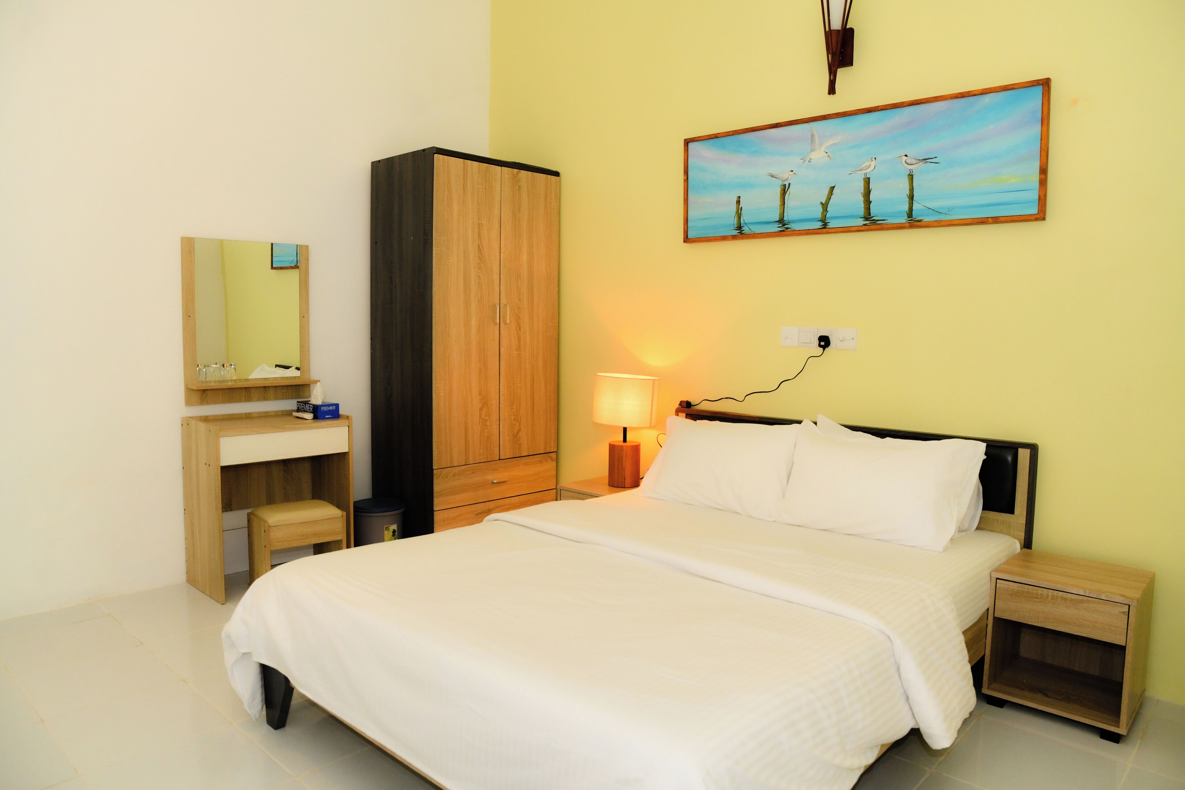 A neatly arranged hotel room with a bed, bedside tables, a desk, a wardrobe, and a painting on the wall.