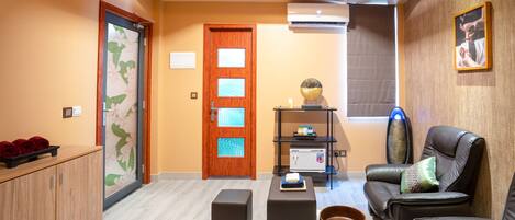 A modern living room with a wooden door, a sofa, ottomans, a small table, and a wall-mounted shelf.