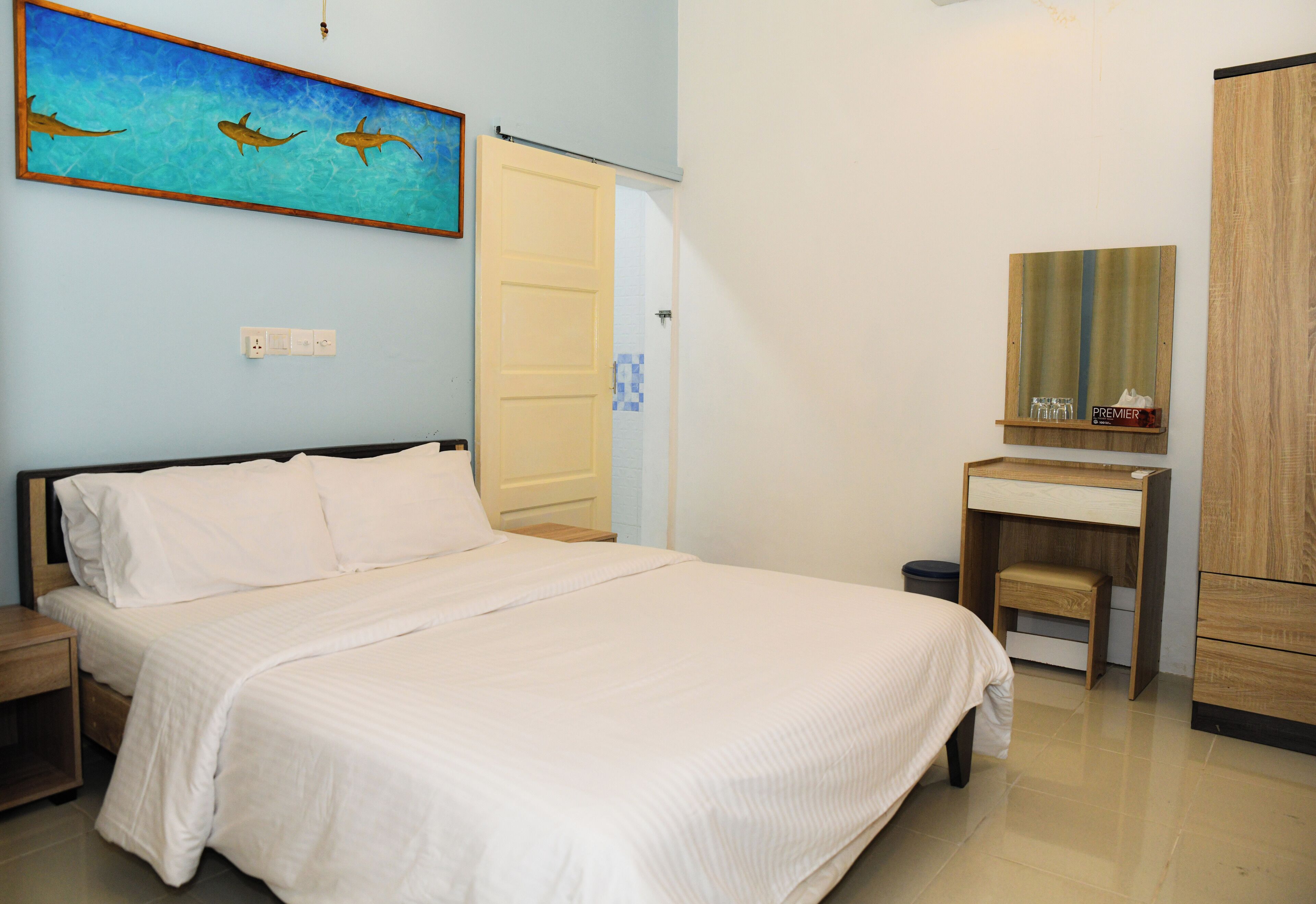 A bedroom with a bed, a nightstand, a desk with a mirror, and a wall-mounted shelf.
