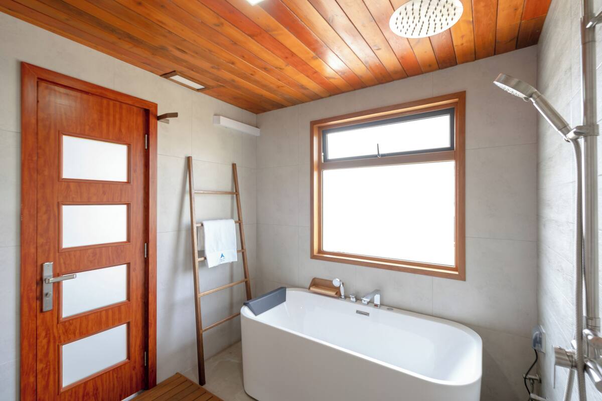 A bathroom with a wooden ceiling, a large window, a bathtub, and a shower.