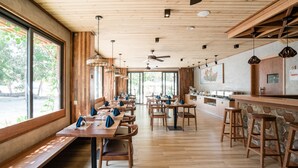 A spacious restaurant with wooden tables and benches, large windows, and a stone accent wall. - Ayala Ocean View (Gulhi)