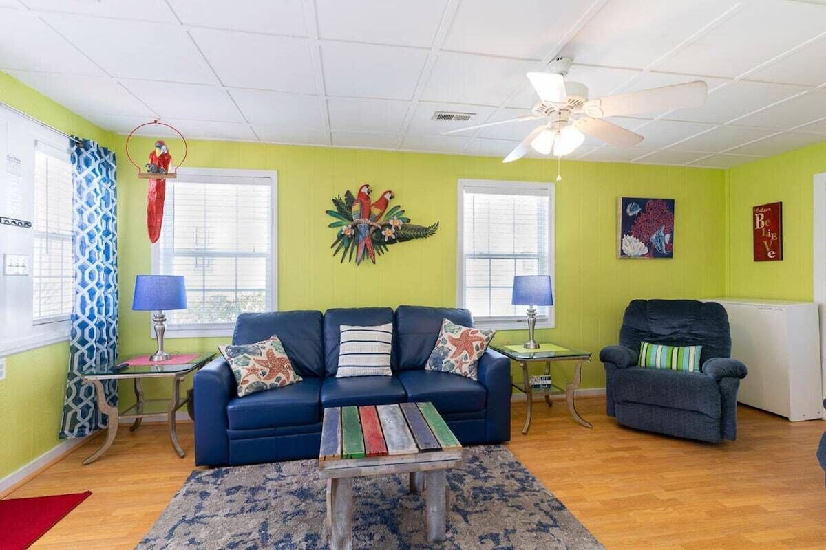 A living room with a blue sofa, a coffee table, a ceiling fan, and artwork on the walls.