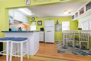 A kitchen with white cabinets, a white refrigerator, and a bar area with stools.