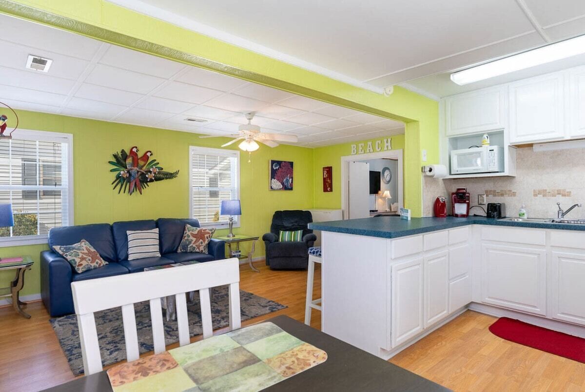 A living room with a blue sofa, a white coffee table, and a kitchen with white cabinets and a blue countertop.
