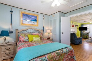 A bedroom with a bed, nightstands, a ceiling fan, and a painting on the wall.