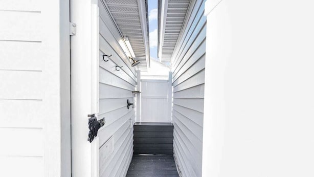 Una escalera estrecha y cerrada que lleva a una puerta con picaporte negro, flanqueada por revestimiento blanco y una barandilla de metal.