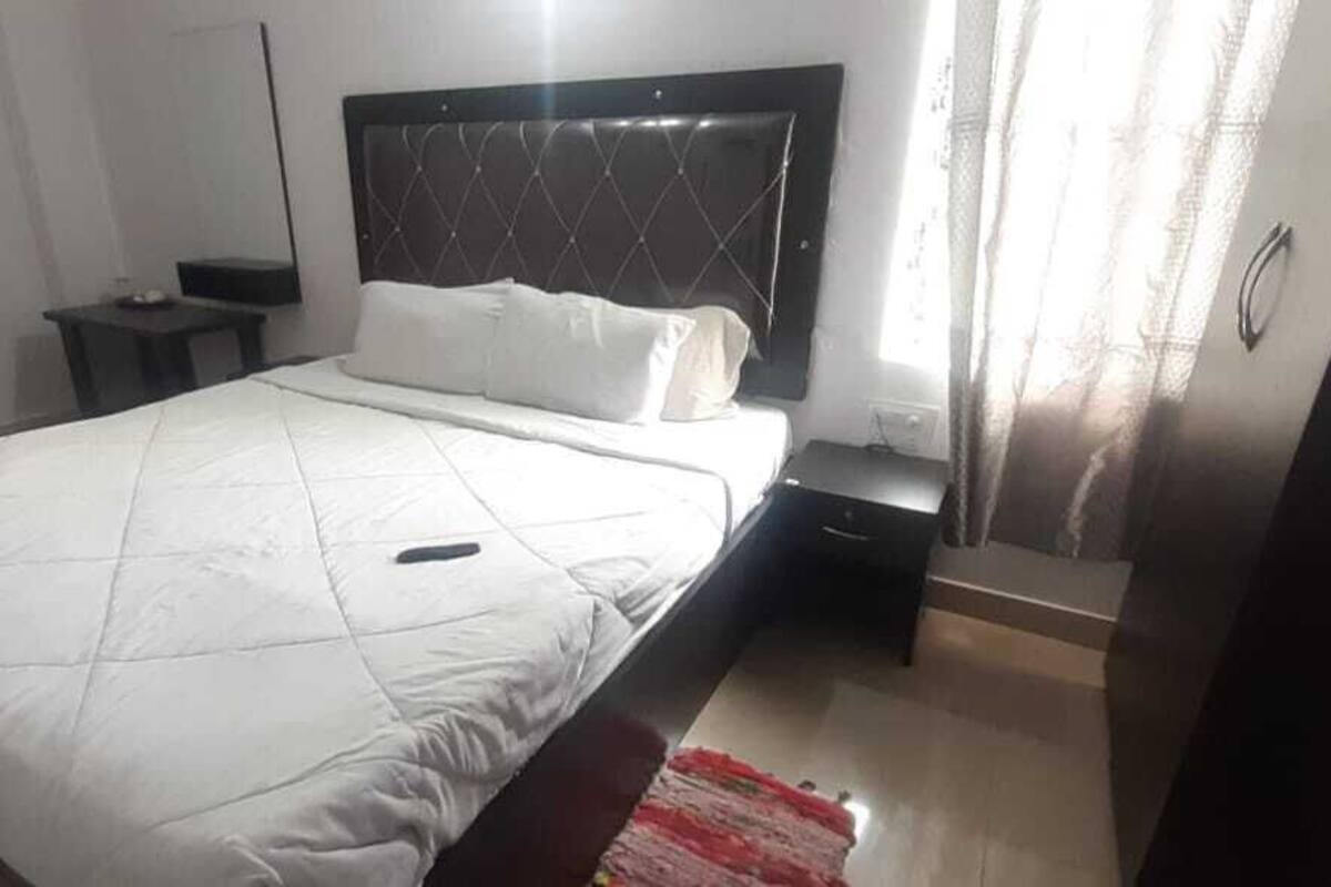 Un dormitorio con cama, mesita de noche, cómoda y ventana con cortinas.