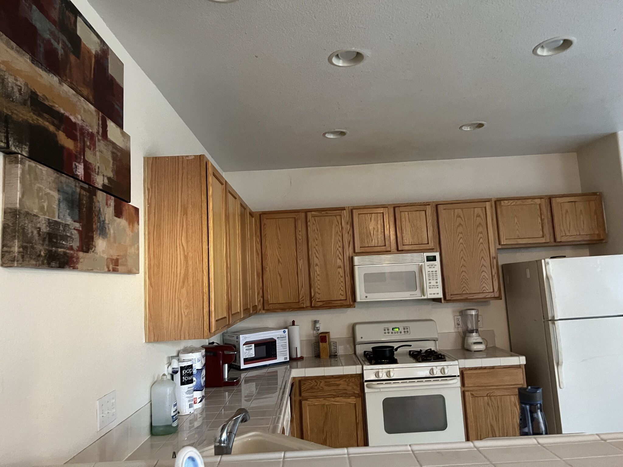 Una cucina con mobili in legno, un forno a microonde, un fornello, un lavandino e un quadro appeso al muro.