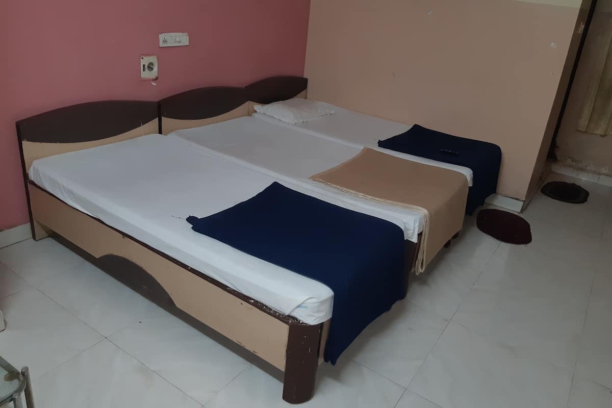 A double bed with a white and blue bedspread, a wooden headboard, and a pink wall.