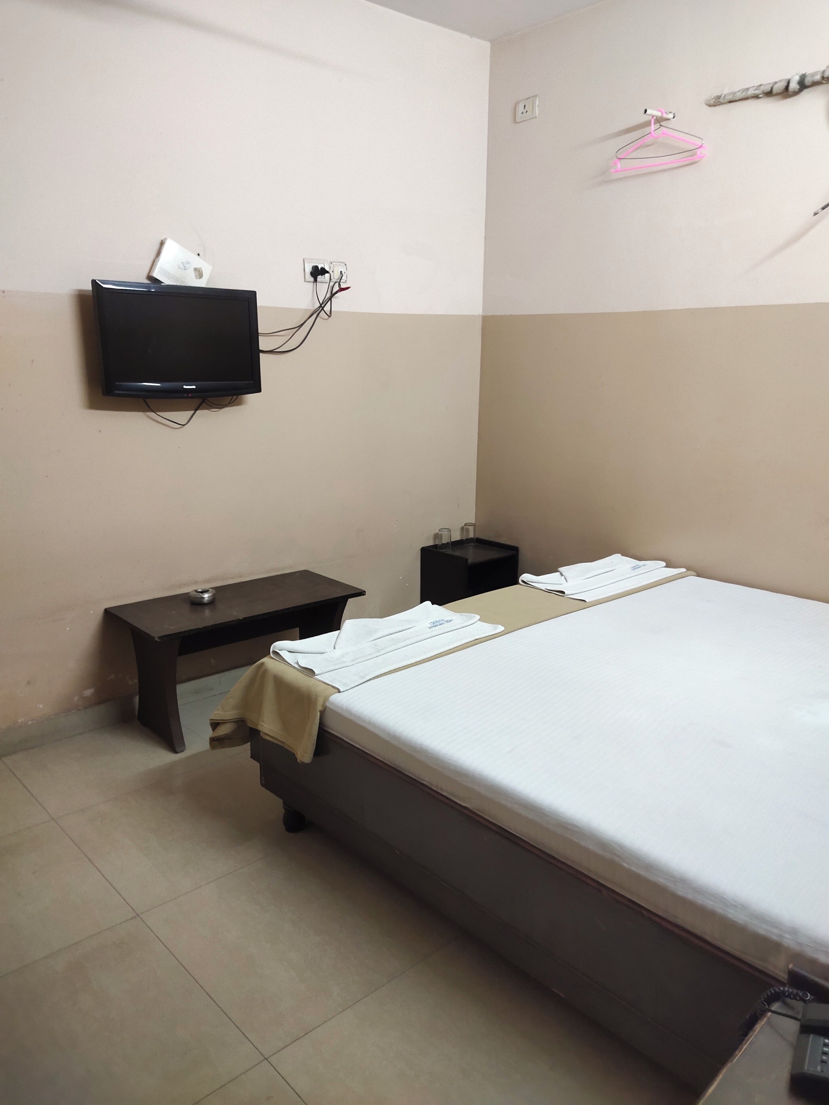 A hotel room with a bed, a bedside table, a TV mounted on the wall, and a small desk with a chair.