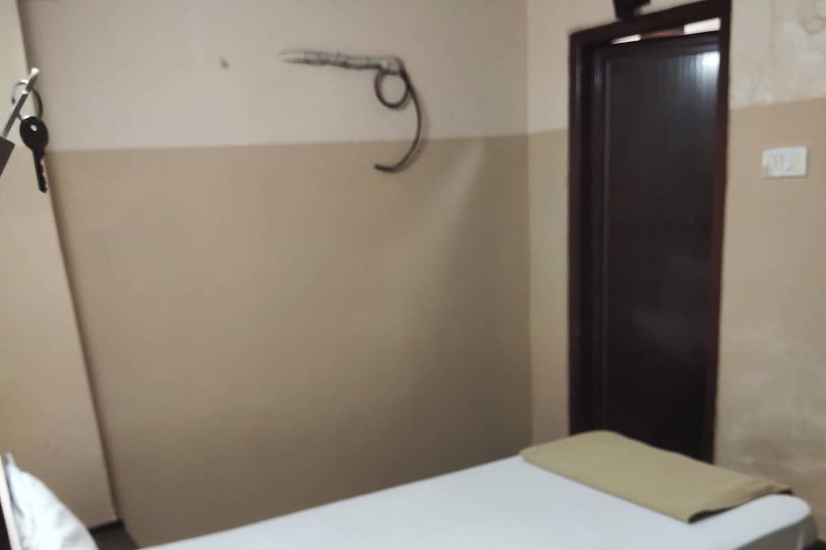 A single bed with a white mattress and a beige blanket, a wooden nightstand, and a dark-colored wardrobe.