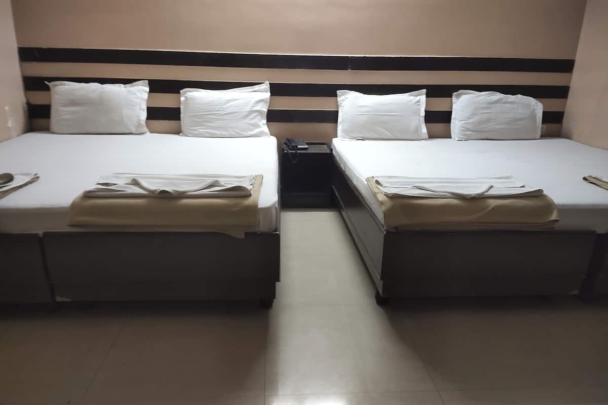 Two single beds with white linens and beige bedspreads, a black and white striped headboard, and a small bedside table with a lamp.