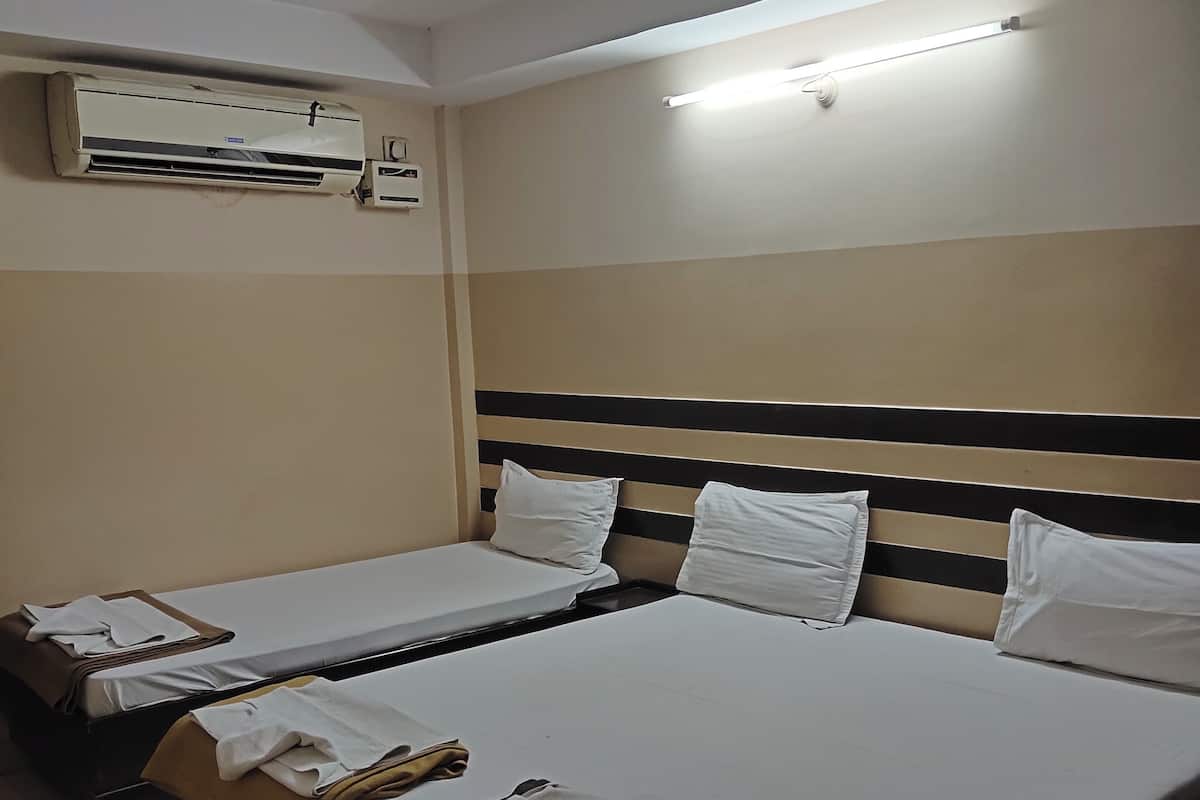 A hotel room with two beds, a ceiling fan, an air conditioning unit, and a wall-mounted light fixture.