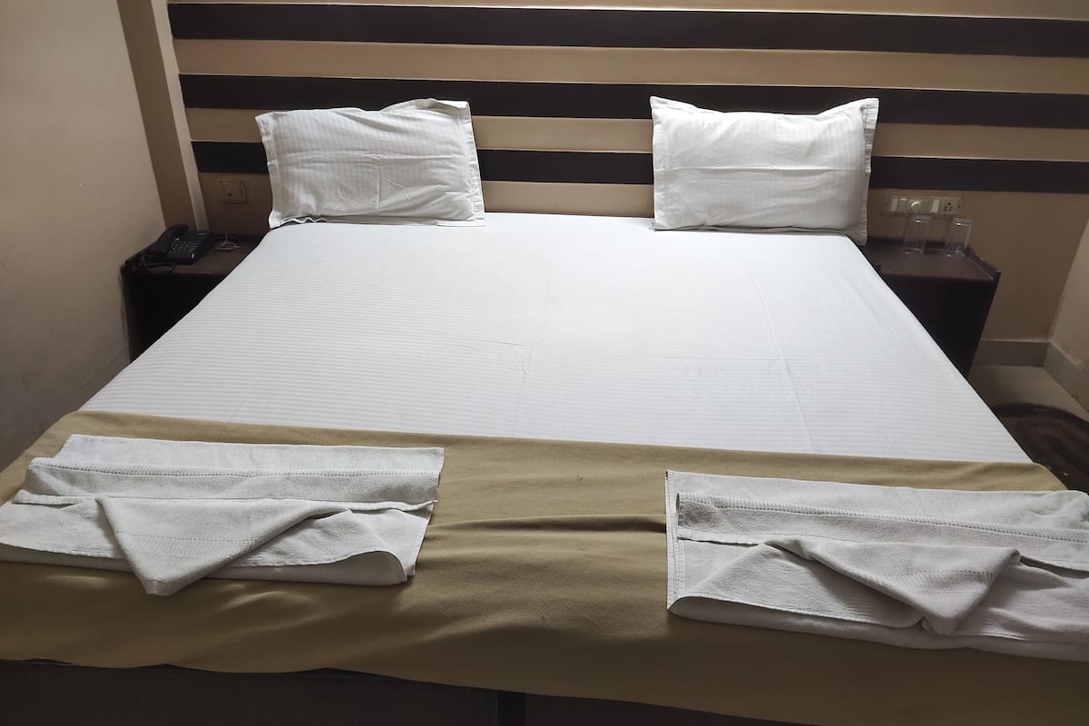 A neatly made bed with white linens, two pillows, and two folded towels on the bed.