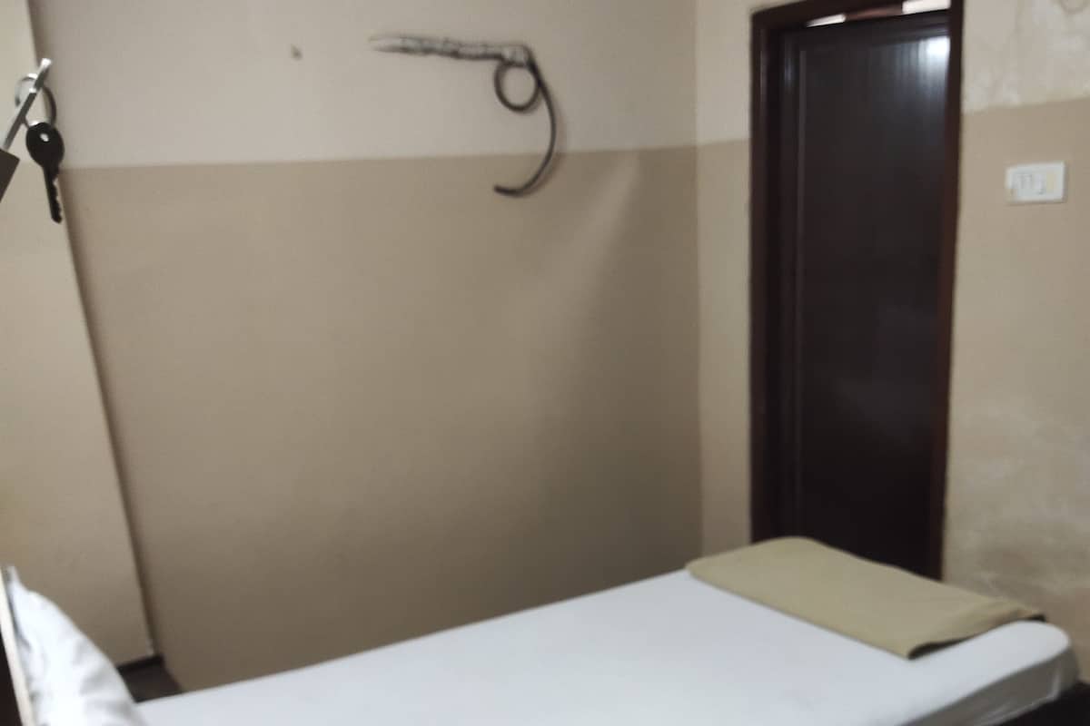 A single bed with a white mattress and a brown headboard, a small bedside table, and a dark-colored wardrobe.