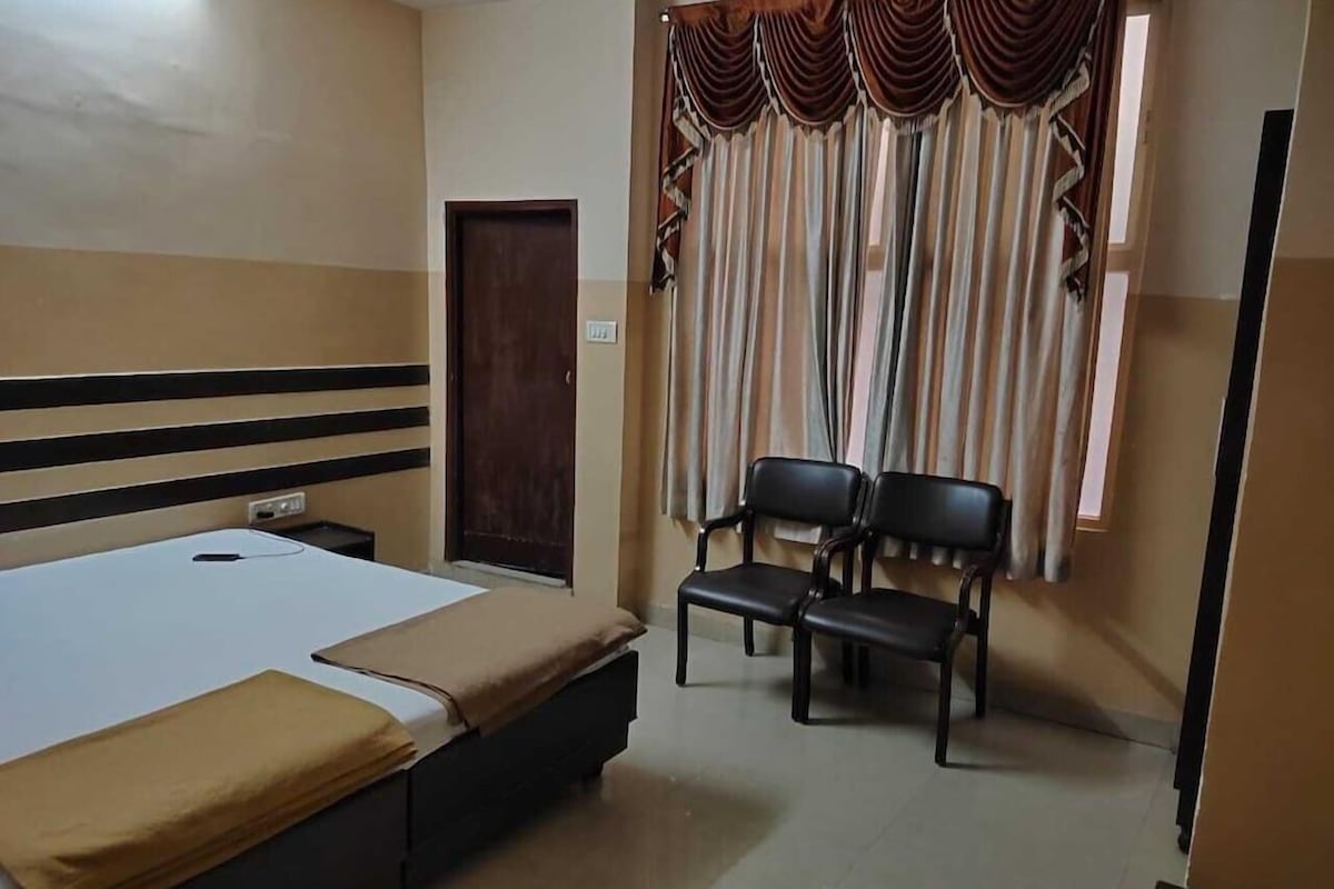A hotel room with a bed, a desk, two chairs, a window with curtains, and a door.