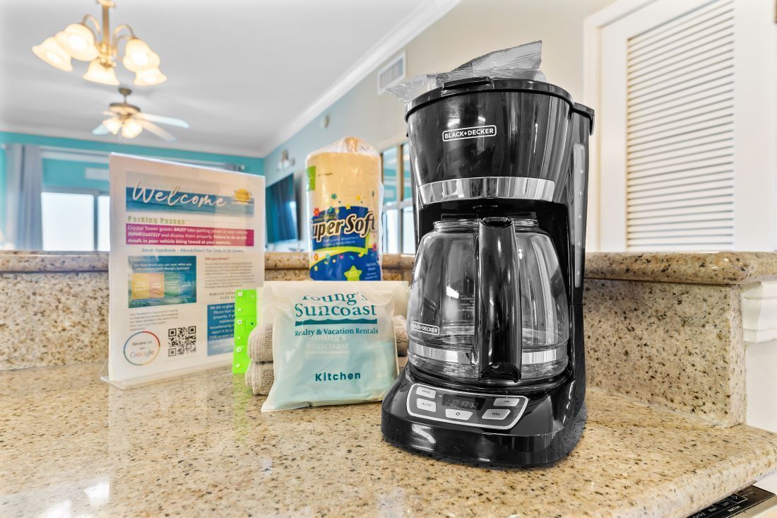 Un comptoir de cuisine avec une machine à café, un paquet de lessive SuperSoft, un paquet de torchons de cuisine Young Suncoast et un panneau d’accueil.