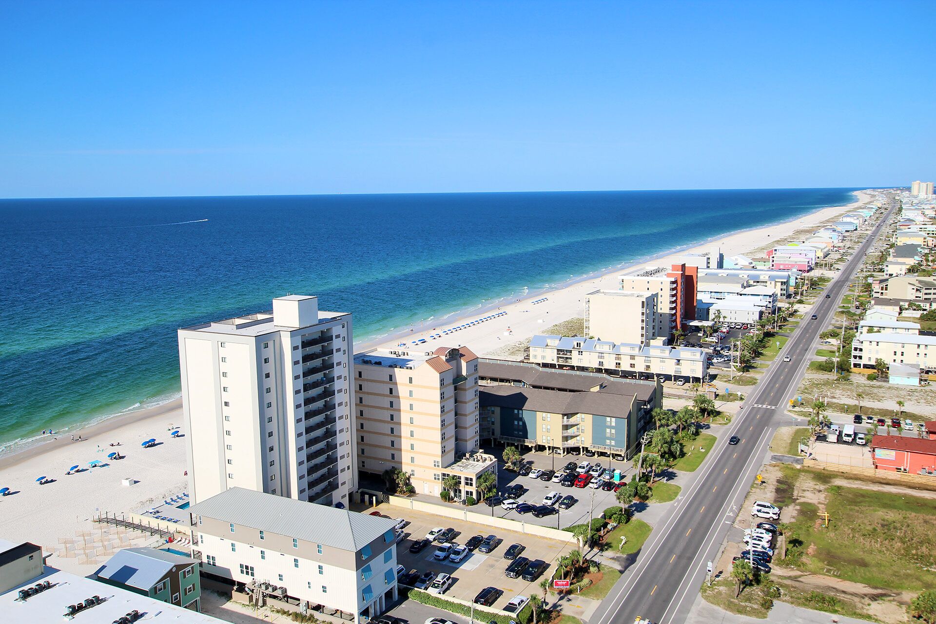 A coastal hotel with multiple floors, a parking lot, and a beach view.