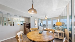 En rummelig spiseplads med et rundt træbord, træstole og en hængende pendel.